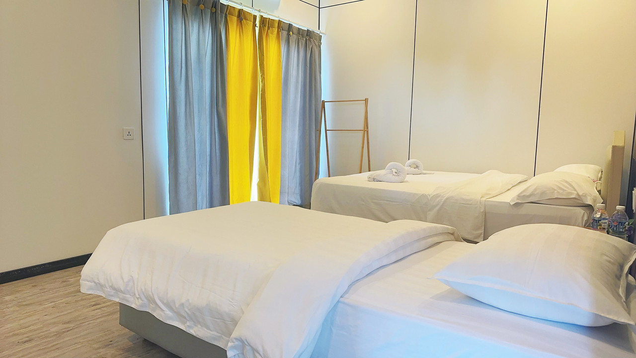A bright family bedroom at Sunny Holiday near Bohey Dulang, showcasing two comfortable beds, modern style decor, colorful yellow and grey curtains, elegant hardwood floors, and A/C.