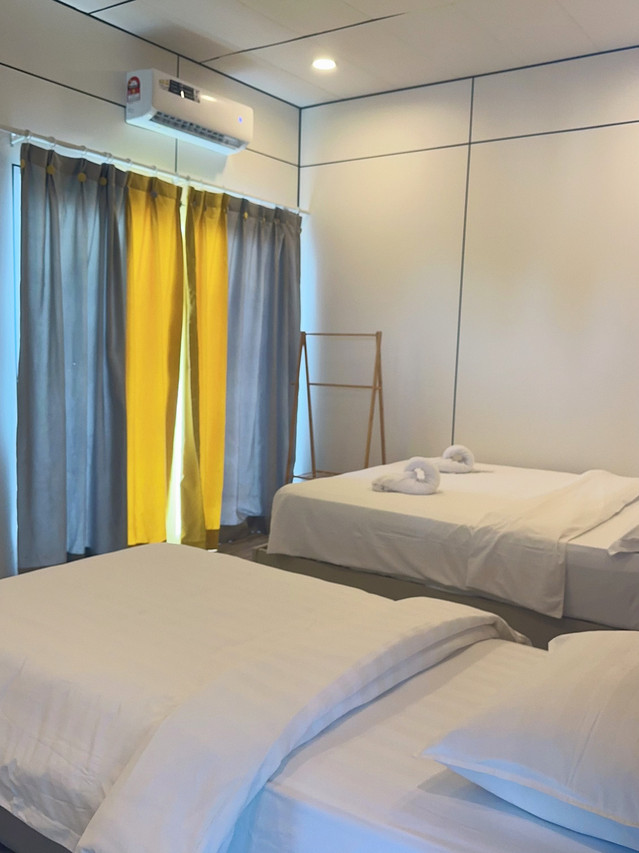 Two comfortable beds inside a family room at Sunny Holiday near the Tun Sakaran Marine Park highlighting folded white towels, elegant blue drapery, a polished teak wood floor, and air conditioning.