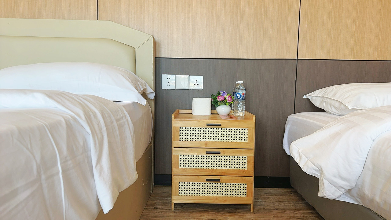 A comfortable family room at Sunny Holiday in the Semporna archipelago, featuring two large beds, a traditional style rattan bedside table, sleek timber floors, and air con.