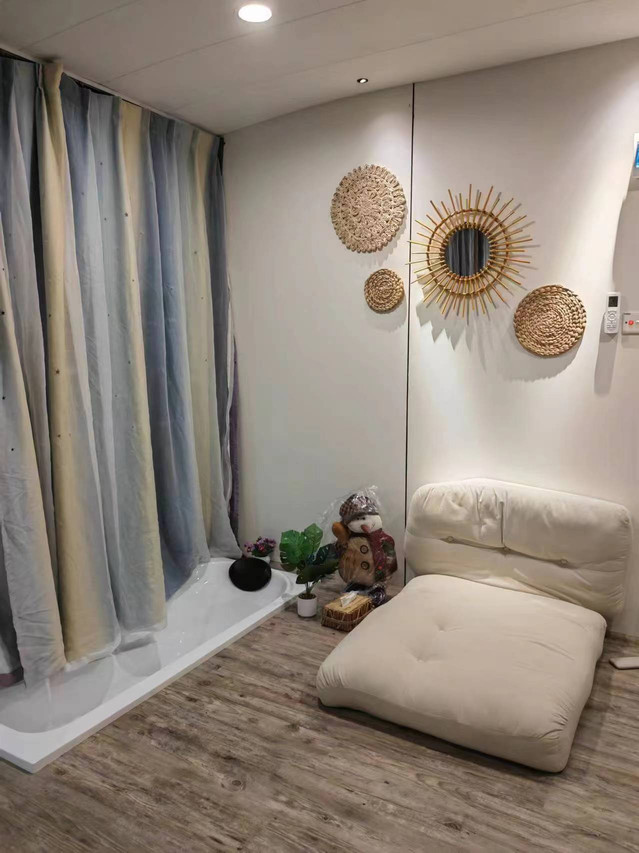 A relaxing bedroom corner at Sunny Holiday near Pulau Bum Bum showcasing a modern style floor lounger next to a sunken bathtub, woven wall art, solid wood floors, and an A/C remote.