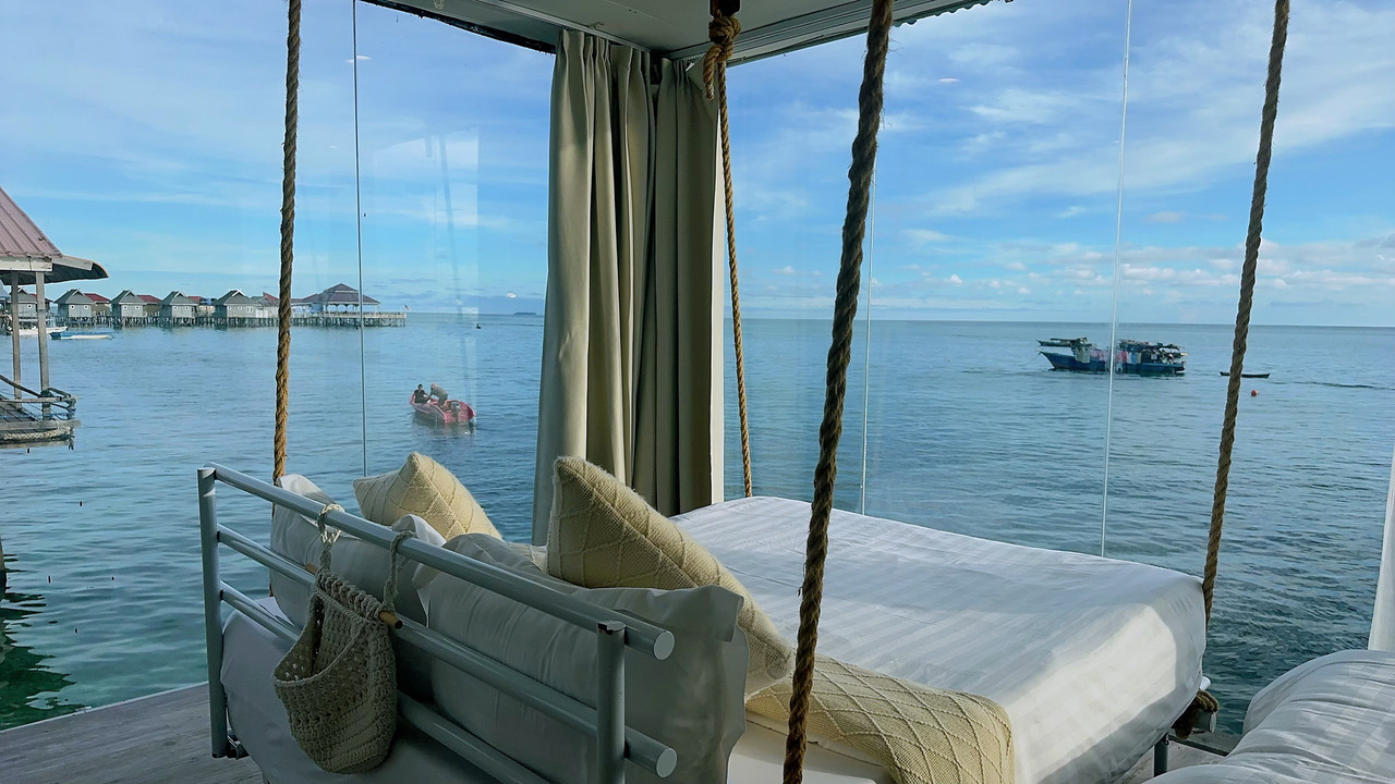 An incredible bedroom at Sunny Holiday in the Semporna archipelago featuring a large swinging bed, traditional style accents, solid timber floors, air conditioning, and panoramic glass windows.