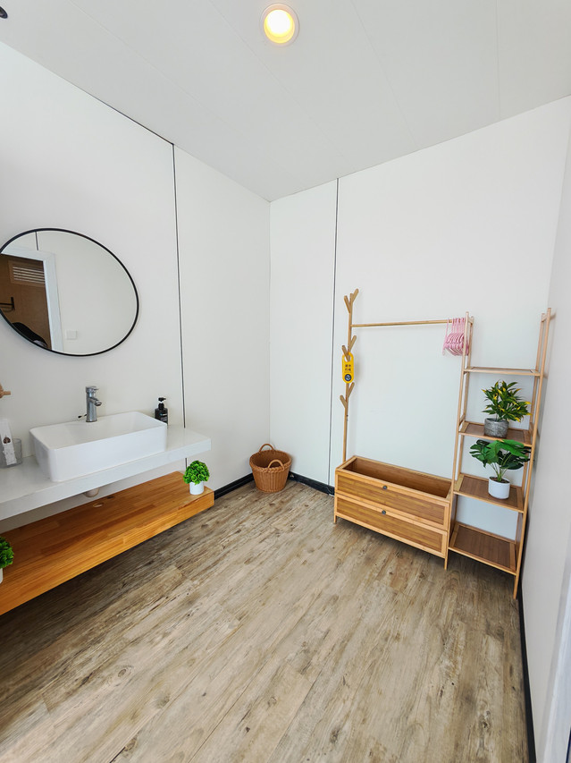 A bright bedroom dressing area at Sunny Holiday in the Celebes Sea, showcasing a traditional style wooden clothing rack, a modern vanity desk with mirror, polished wood floors, and AC.