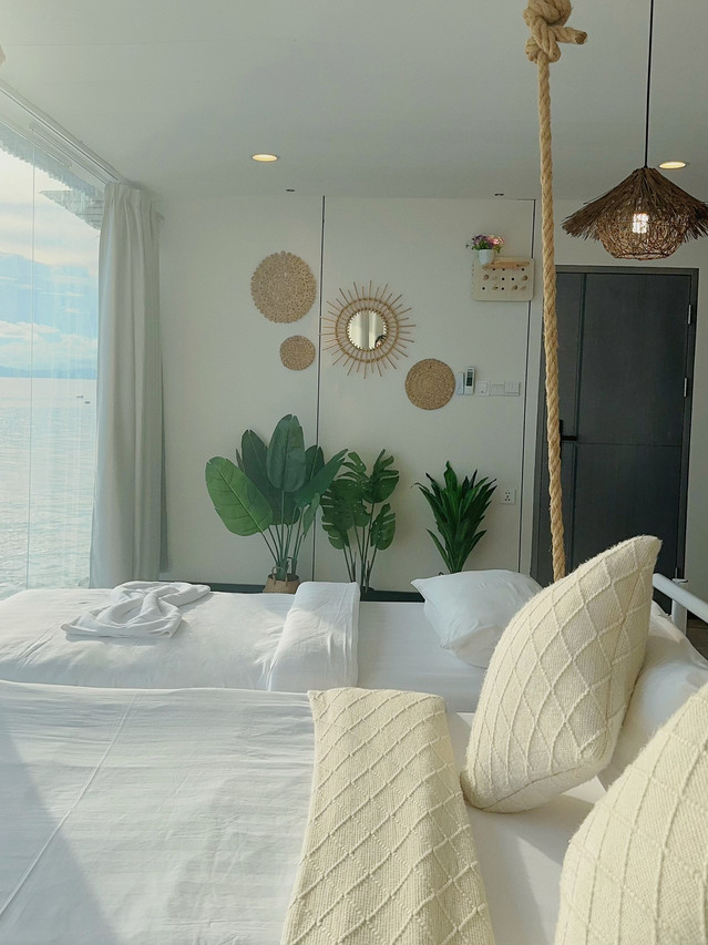 A plush bed inside a bright bedroom at Sunny Holiday in the Celebes Sea featuring blue headboard drapes, facing glass doors with partial ocean views, authentic timber floor boards, and air con.