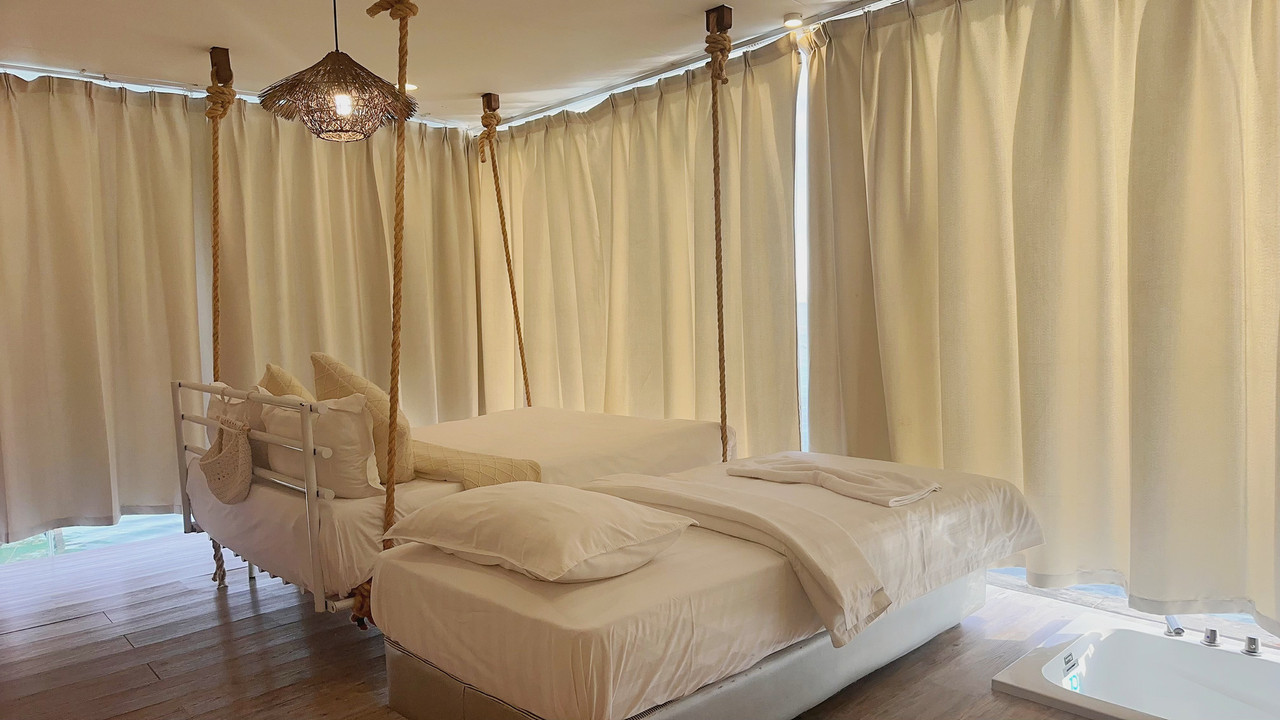A comfortable bedroom at Sunny Holiday in Semporna featuring a large swinging bed and a single bed, traditional style curtains, a sunken bathtub, elegant hardwood floors, and air con.