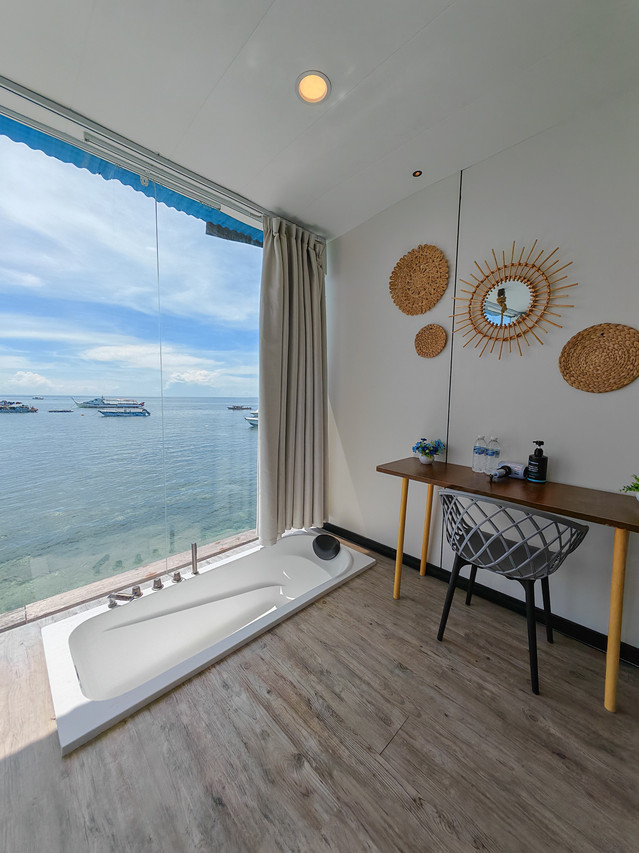 A sun-drenched bathroom featuring an in-floor soaking tub next to a floor-to-ceiling glass wall with a panoramic ocean view at Sunny Holiday.