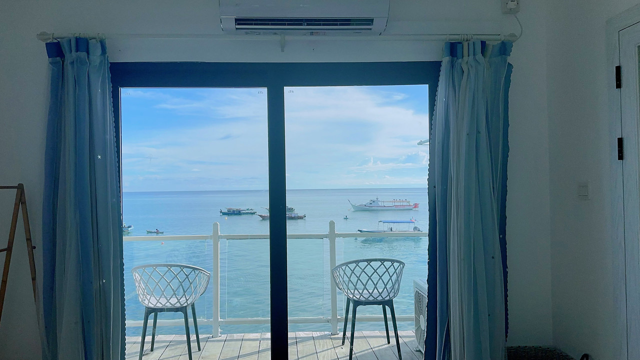 A relaxing bedroom at Sunny Holiday near Bohey Dulang offering modern style blue curtains, solid wood floors, AC, and panoramic glass doors opening onto the balcony overlooking the sea.