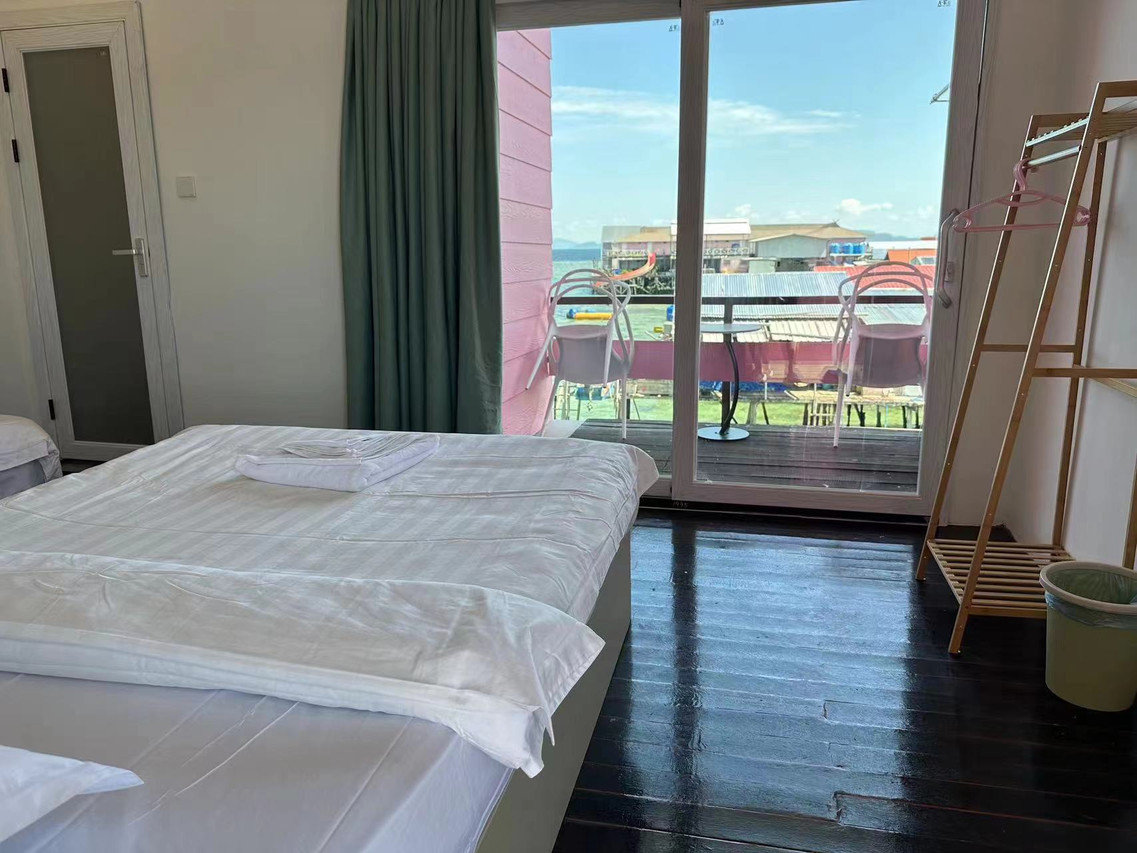 A cozy bedroom at Sunny Holiday over the Celebes Sea featuring a king size bed, modern style clothing rack, dark polished wood floors, AC, and sliding glass doors opening onto the balcony.