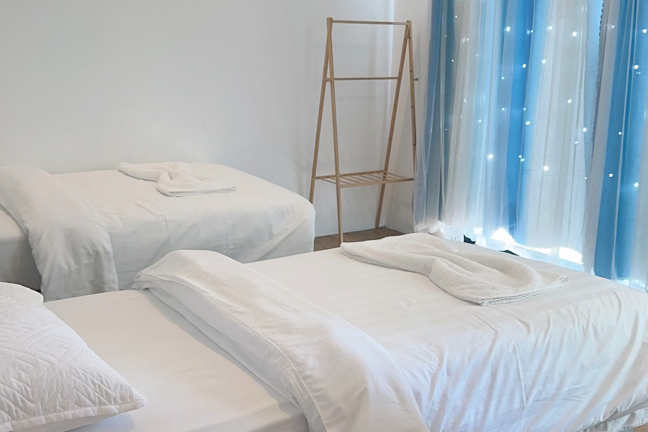A bright bedroom at Sunny Holiday in Semporna featuring two large beds, modern style decor, smooth wooden floors, starry blue curtains, and AC.
