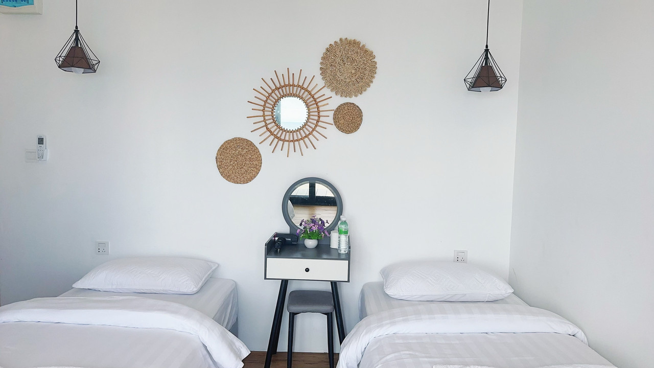 A cozy bed inside a bright bedroom at Sunny Holiday near Semporna detailing pink folded towels, elegant blue headboard drapery, a smooth varnished timber floor, and A/C.
