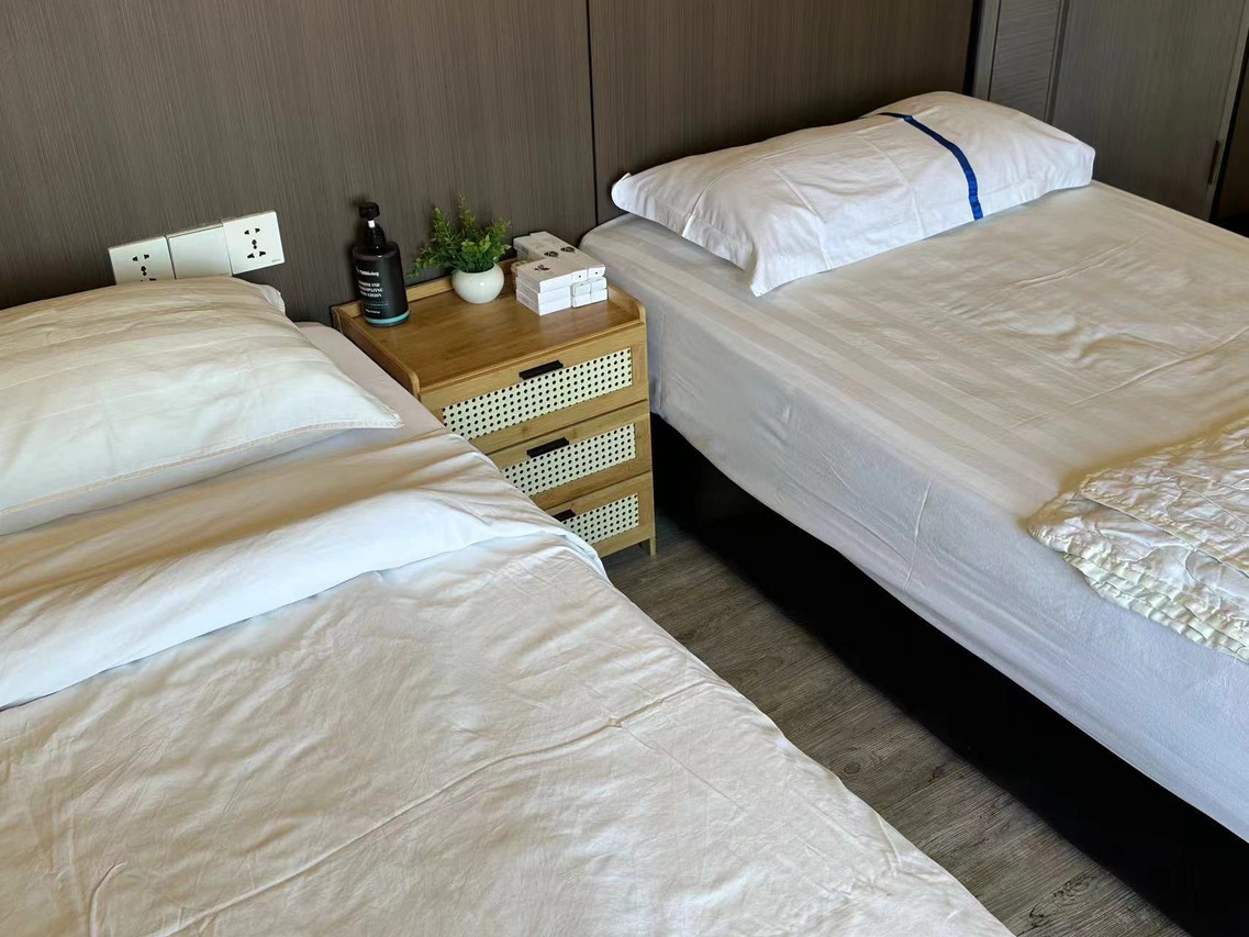 A cozy twin bedroom at Sunny Holiday in the Semporna archipelago showcasing two large beds, a traditional style rattan nightstand, sleek timber floors, and air con.