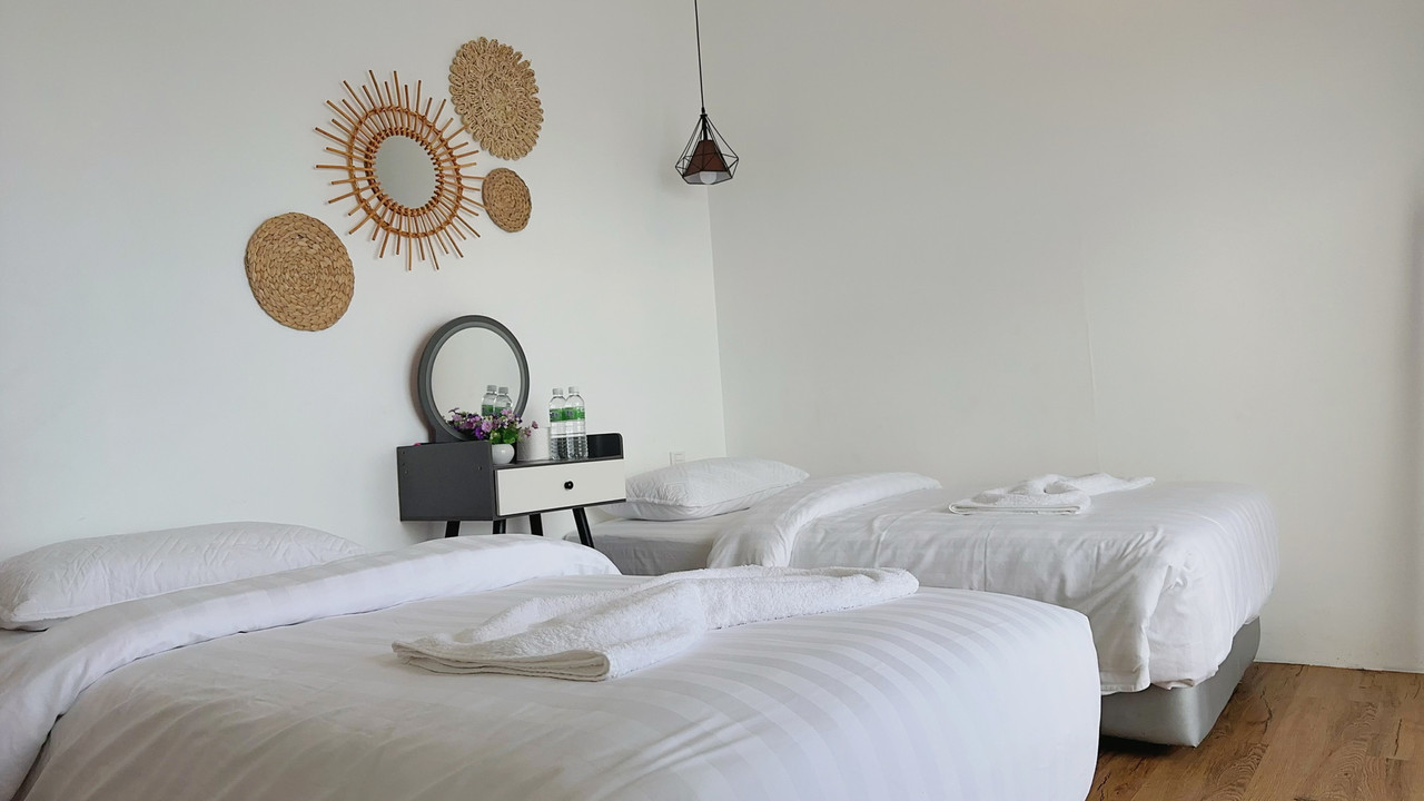A bright bedroom at Sunny Holiday in the Islands of Semporna featuring two large beds, a modern style vanity desk, woven wall art, smooth wooden floors, and air conditioning.
